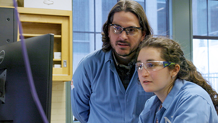 Two people in lab gear looking at computer screen