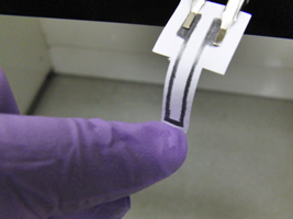 A strain gauge made of pencil and paper is deformed to compress the graphene network.