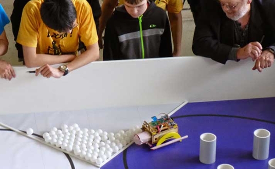 A crowd watches one of the autonomous robots attempt to pick up Ping-Pong balls during the 2014 Design Competition.