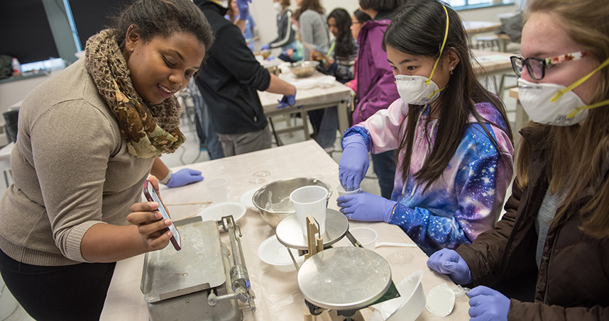 With help from a graduate student, girls complete an experiment to learn about chemical reactions.