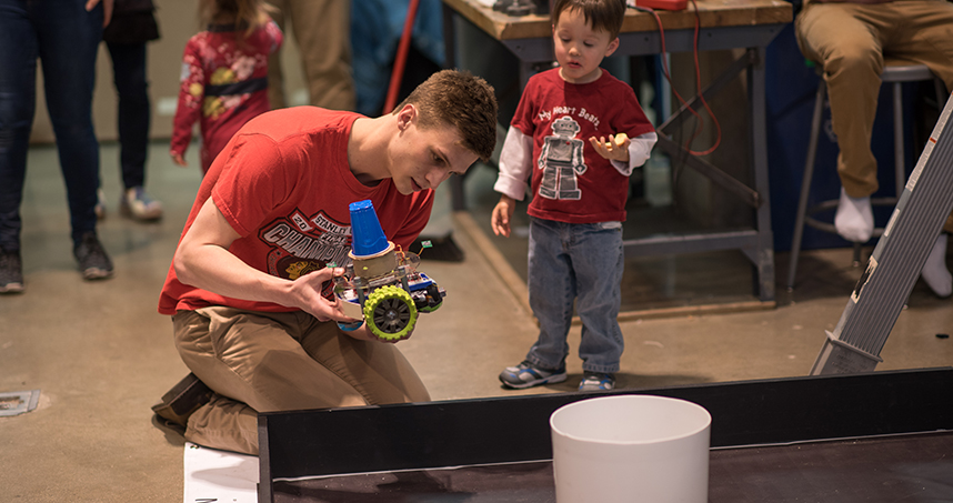 A small visitor watches a student get his robot ready for the competition.