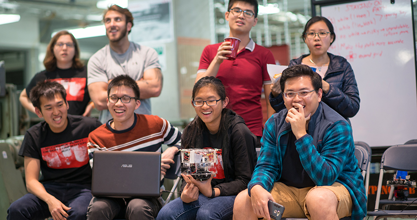A student team laughs and cheers while watching the competition perform in the arena.