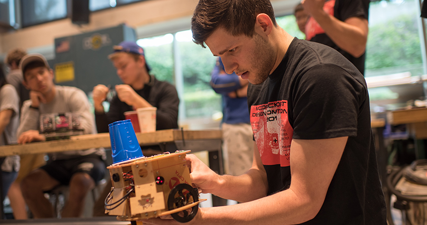 A student gets his robot ready, which includes placing the plastic cup target on its top.