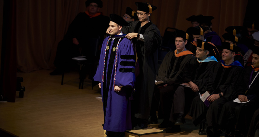 A PhD candidate receives his hood from his advisor