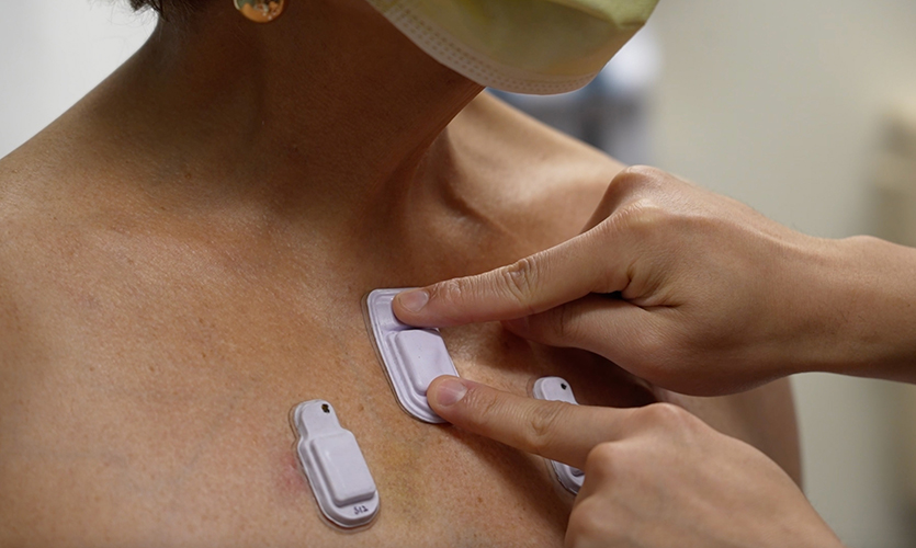 A health care worker sticks wearable devices onto an adult patient's chest. 