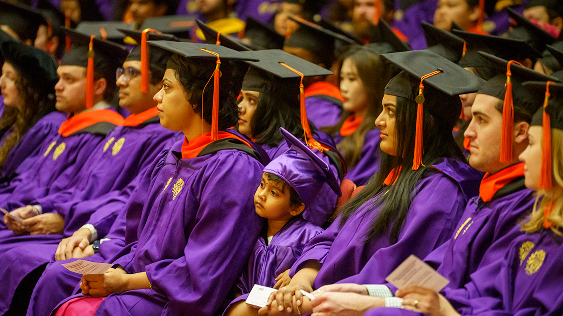 The graduates, and one youngster, listen to one of the speeches.
