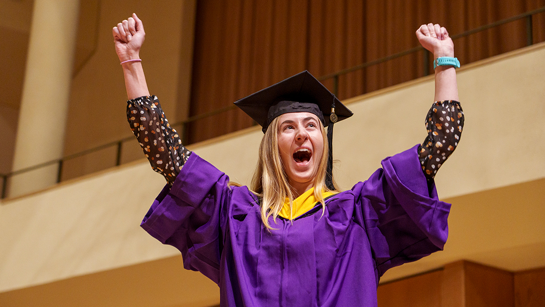 A graduate celebrates as she is about to walk across the stage.