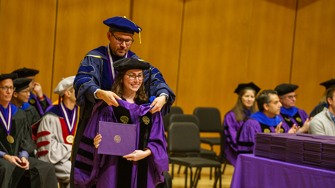 Professor Joshua Leonard places a hood over a new PhD.