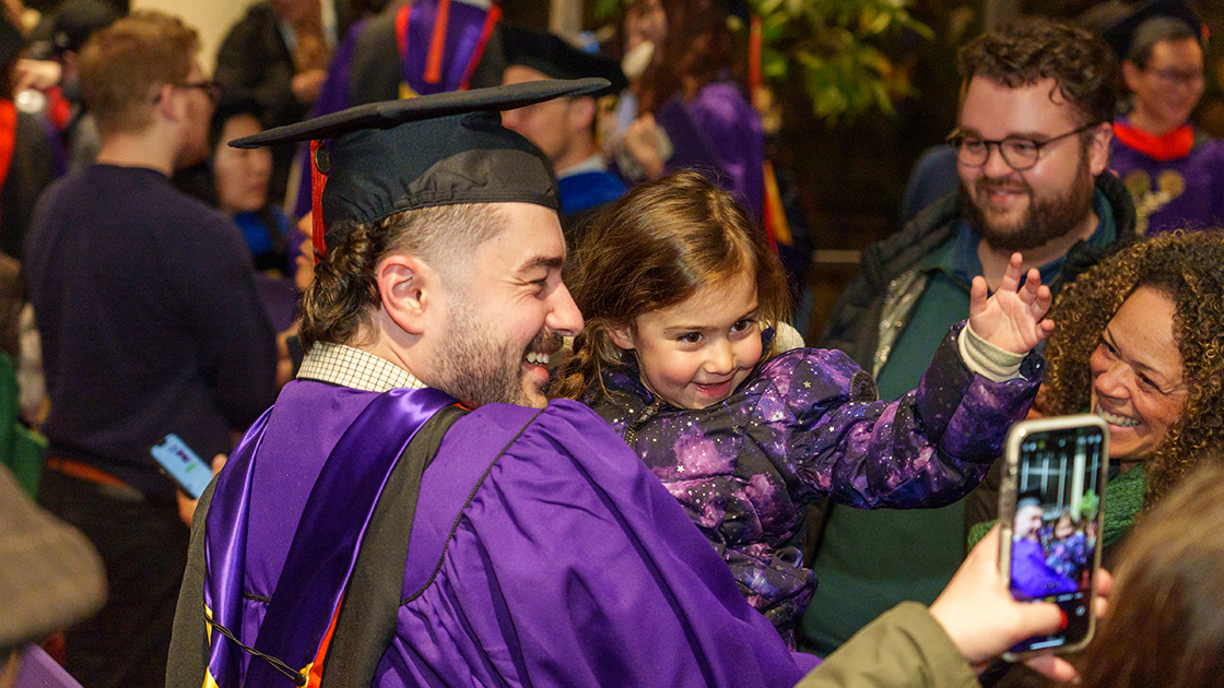 A new graduate poses for a photo holding a young child.