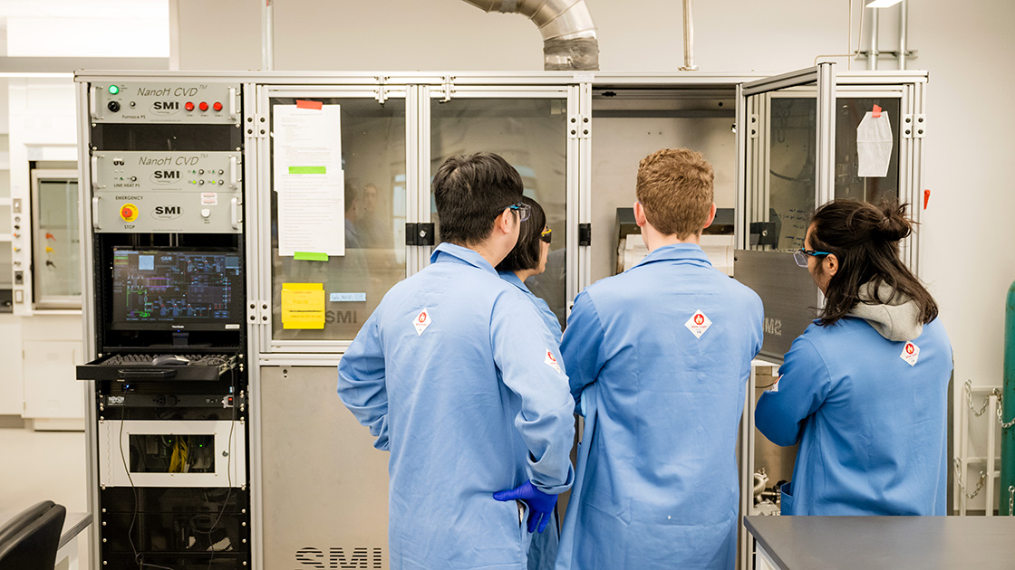 Students gather around the Metal-Organic Chemical Vapor Deposition to view a sample.