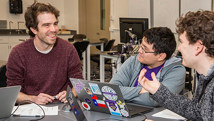 Three people in discussion around laptops