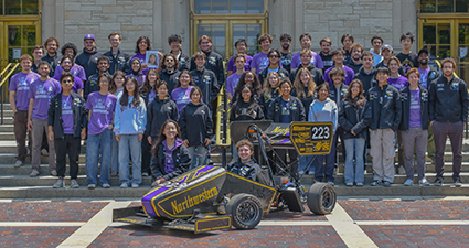 Group of students standing in front of the Tech building with their racing car